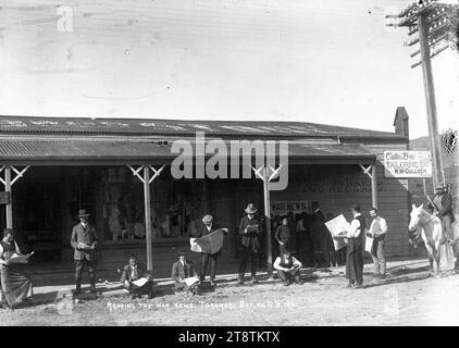 People reading the war news in Tokomaru Bay, Group of men (including two shop assistants) reading the war news outside the general store in Tokomaru Bay. A group of children and a male teacher are standing on the verandah gathered around the `War News' noticeboard. The shop front window displaying items of clothing can be seen behind the men in the centre of the photograph. Sign on the righthand side of the store reads `Oates Bros, Tailoring Dept. W. McCulloch, manager', ca 1915 Stock Photo